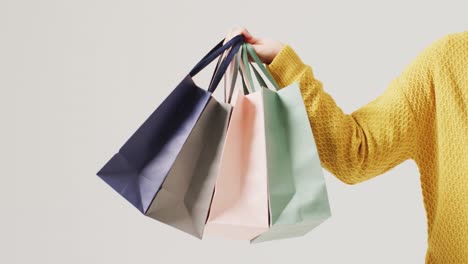 Arm-of-woman-holding-coloured-gift-bags-on-white-background