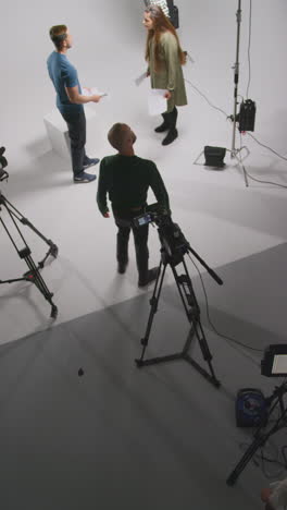 vertical video overhead shot of actors rehearsing movie or video scene in studio with film camera and lighting crew