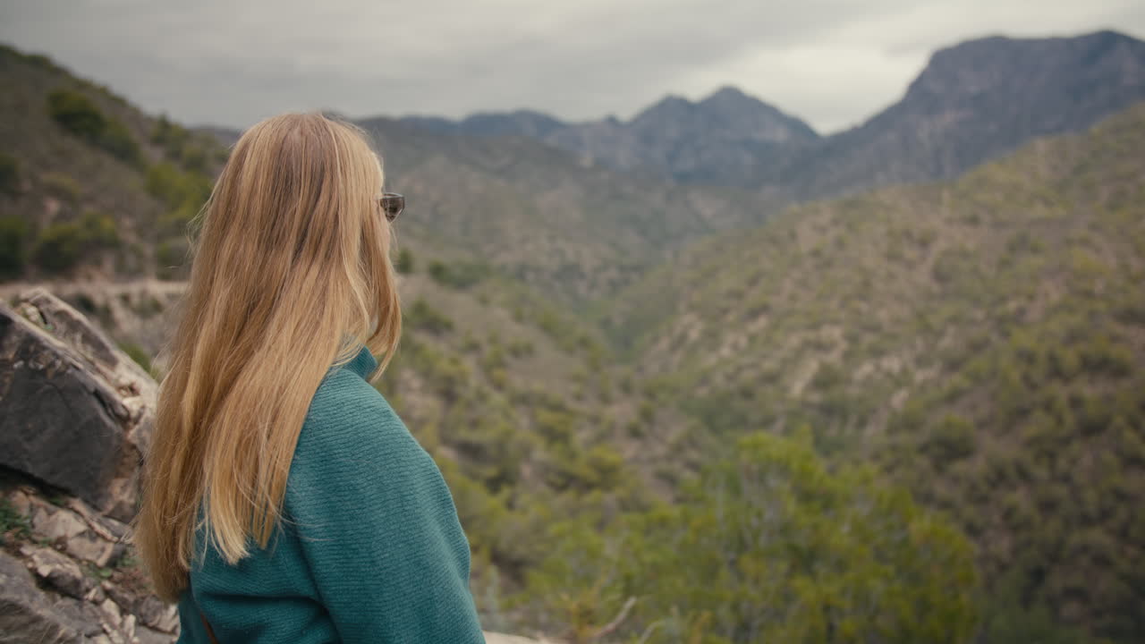 Woman sits resting and looks over a peaceful mountain valley during a cloudy day in southern Spain