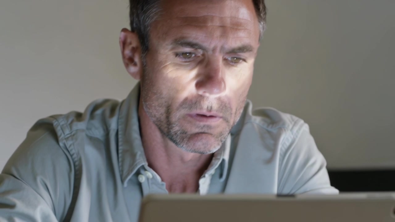 Auf die Uhr schauen: Mann mittleren Alters bewegt den Arm und beugt sich vor, um ein Tablet am Schreibtisch in hellem Hemd zu lesen.