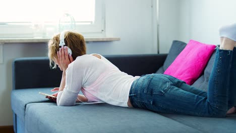 woman is lying on the couch and listening to music