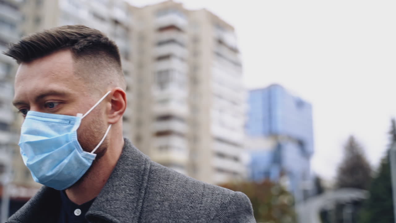 Man tourist protecting face from viruses. Handsome man wearing medical face mask prevents coronavirus while walking in city outside. Slow motion.