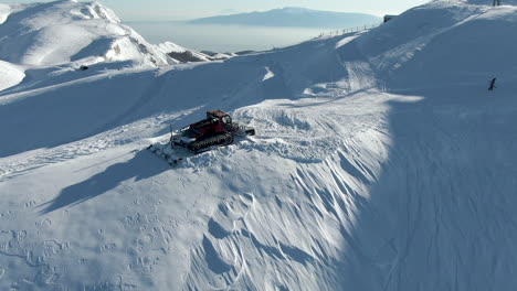snow groomer standing on top of snowy mountain ridge on large ski resort amidst amazing landscape