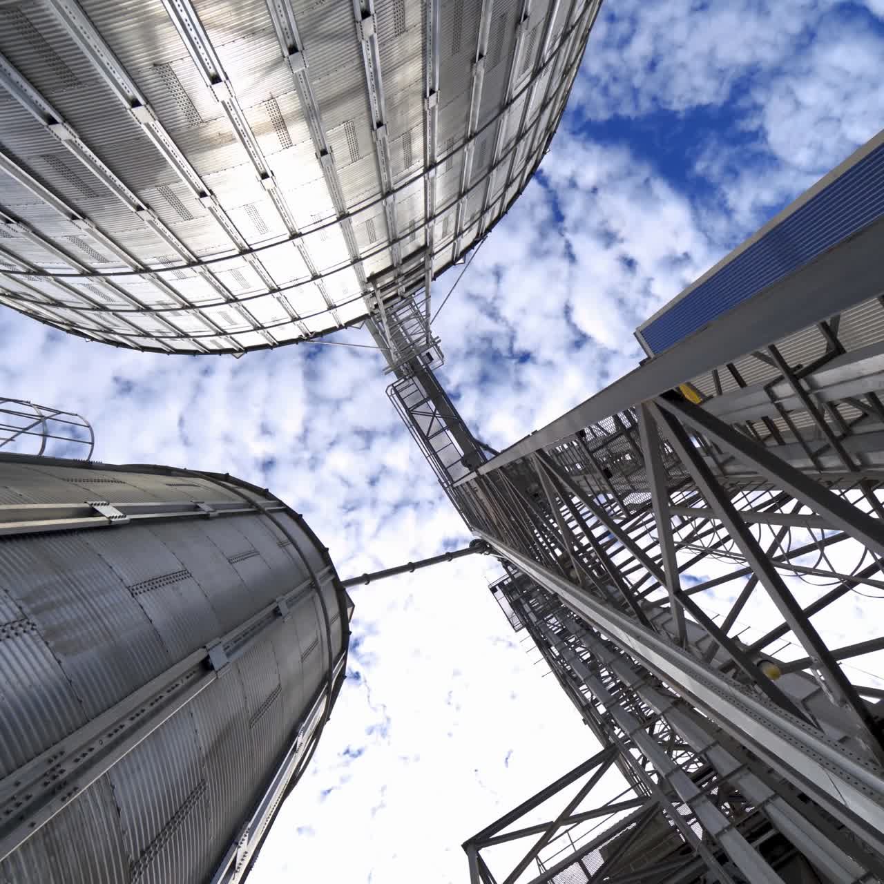 Large industrial plant with storage tanks. Silver grain elevators for agribusiness. Modern warehouse. View from below. Camera circling.