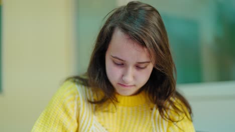 portrait of a school girl at school. teenage student girl in yellow sweater sitting in the classroom and studying. education concept.