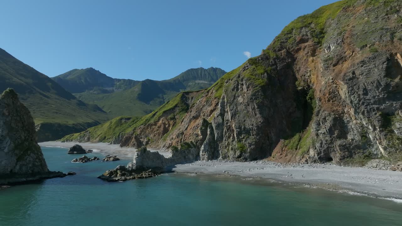 Riprese aeree della costa frastagliata della Baia di Avacha con acqua turchese, faraglioni rocciosi e verdi montagne vulcaniche sotto un cielo sereno nel Krai di Kamchatka, Russia