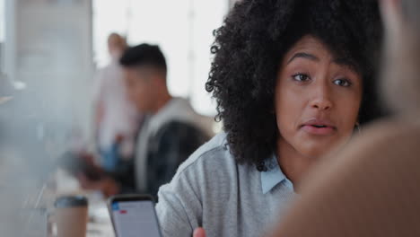 young mixed race business woman manager using smartphone training intern pointing at screen sharing feedback discussing ideas with colleague in office