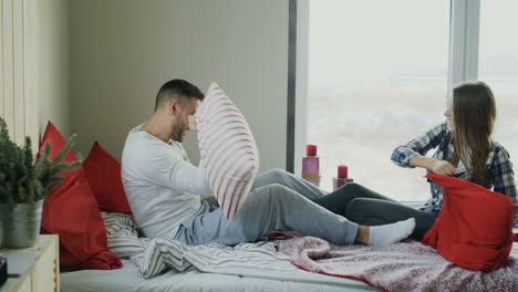 pareja teniendo una pelea de almohadas en la cama