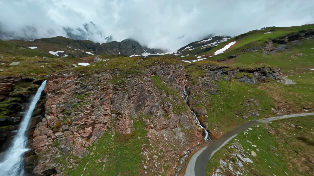 A winding mountain road with a waterfall near Cervinia on a lush summer day