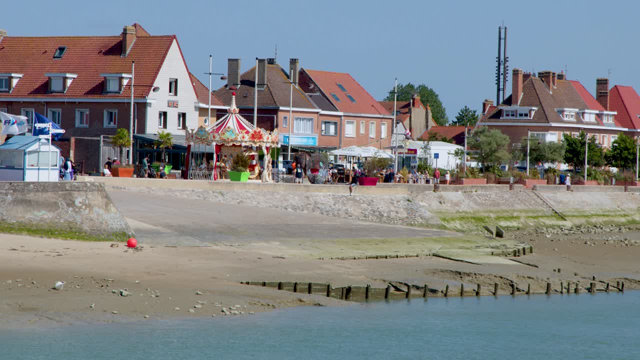 Daytime camera pan reveals beach, carousel, and waterfront buildings under clear blue sky