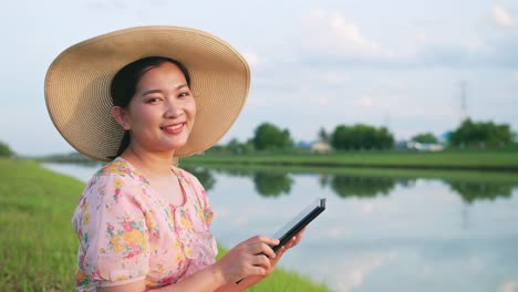 ritratto di bella donna asiatica con cappello che guarda l'obbiettivo utilizzando un dispositivo portatile