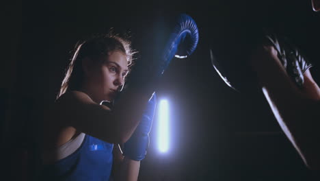 medium shot of beautiful fitness woman boxer treneruemsya strike speed focus mitts with a coach in a boxing club. slow motion