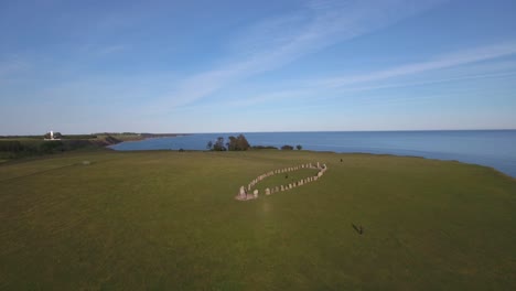 Turistas-Caminando-Alrededor-De-Ales-Stenar-Con-Distancia-Social-En-La-Cima-De-La-Colina-En-Las-Noches-De-Verano-En-El-Sur-De-Suecia-Skåne-Österlen-Kåseberga,-Avance-Aéreo