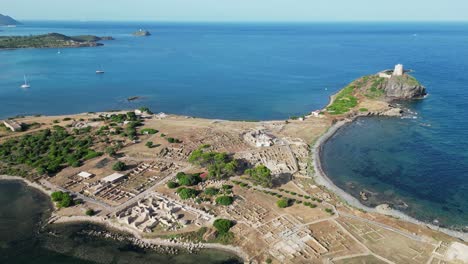 nora peninsula and archeological site with ancient roman ruins in sardinia, italy - aerial backwards