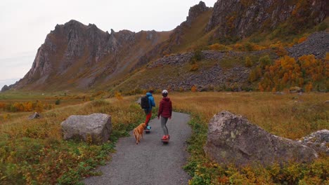 a couple riding one-wheel boards with a dog walking along a scenic mountain path