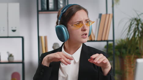 Caucasian-businesswoman-wearing-headphones-listening-music-dancing-after-working-on-laptop-at-office