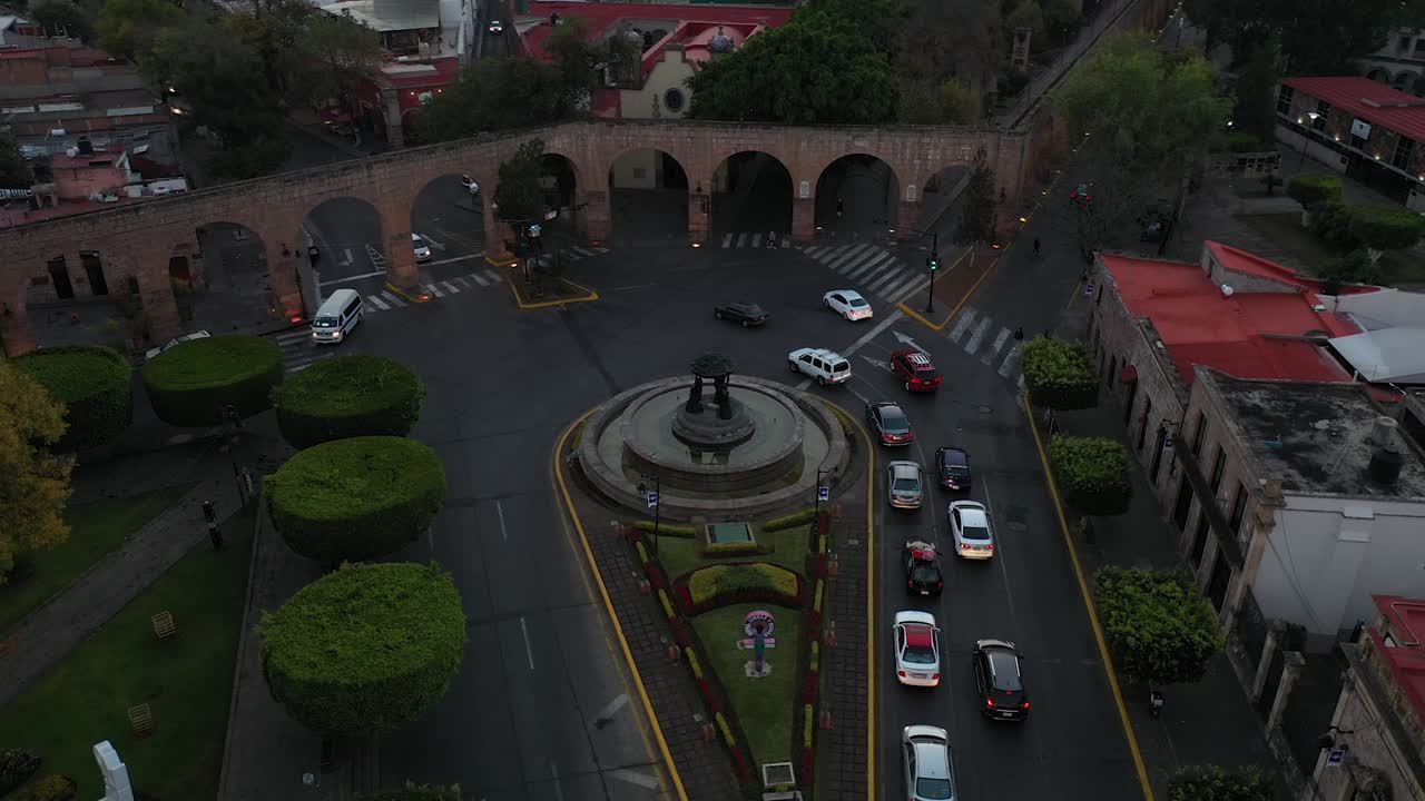 Drone view of the iconic Tarascas Fountain in Morelia, Michoac&aacute;n, with cars circling the roundabout and the city's famous aqueduct arches
