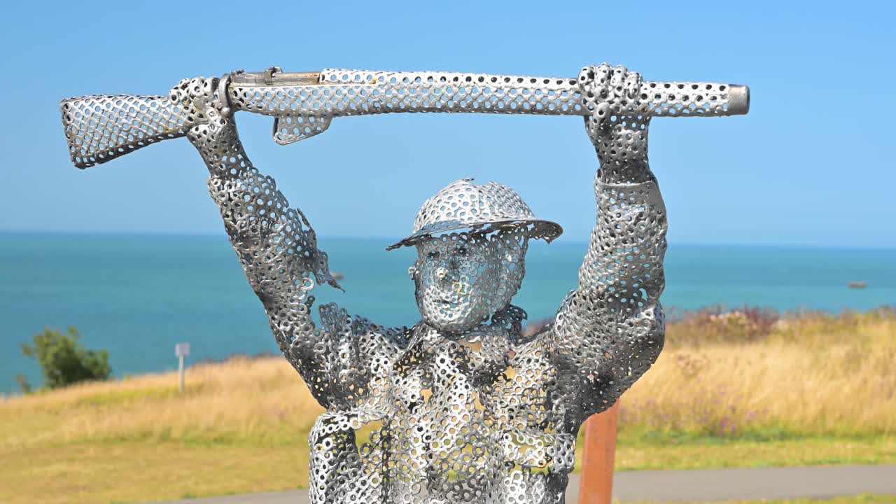 Tourists walking among the metal soldier statues in Arromanches on a sunny afternoon, highlighting the strong bond between history and present-day visitors