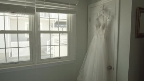 Pull-Back-Shot-of-Brides-Wedding-Shoes-and-Dress-Hanging-by-a-Window-in-the-Bridal-Suite