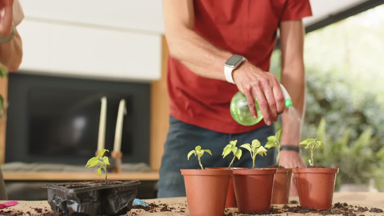 Una coppia guarda un uomo in maglietta rossa che prende uno spruzzino verde e nebulizza vasi di terracotta per innaffiare a casa.