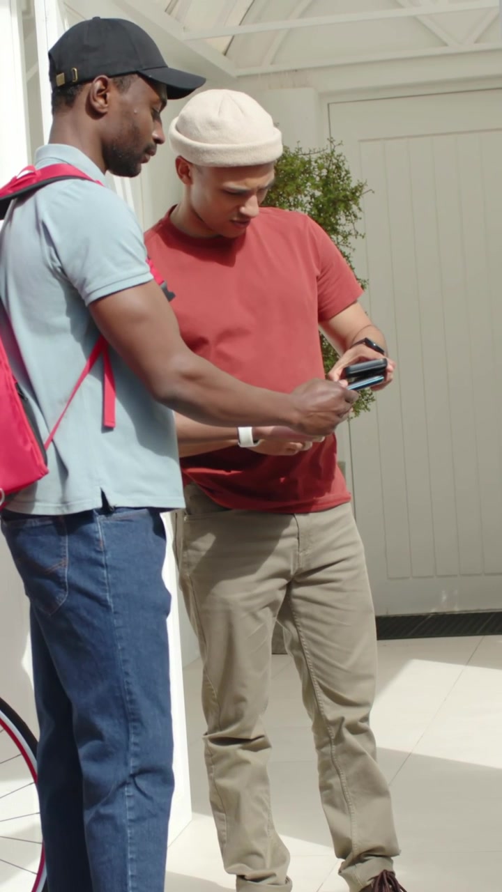 Vertical video: Extending device courier and resident tapping, confirming drop at door red backpack