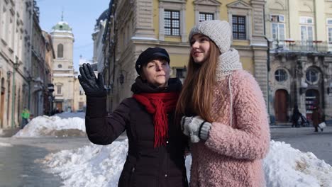 two smiling women tourists walking together on city street, family couple talking, embracing