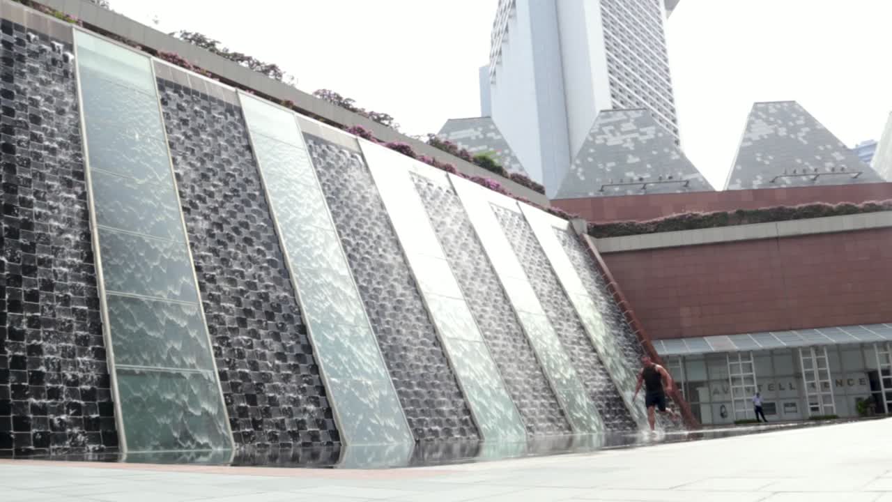 Hombre corriendo a través de una fuente de agua en la Torre Millenia en el distrito de negocios de Singapur