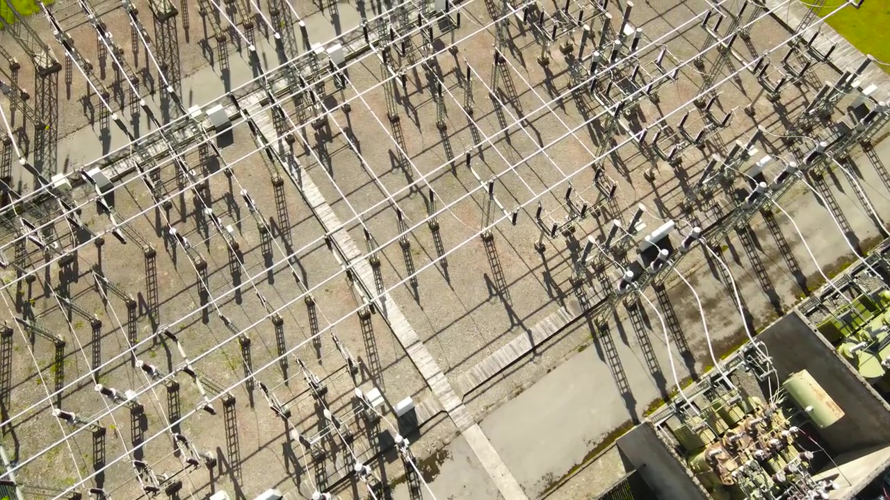 Aerial perspective of a large electrical substation with a complex network of high voltage insulators, cables, and transformers distributing power, showing the grid infrastructure