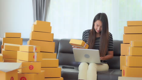 Picking-up-a-small-cardboard-box-a-woman-working-on-her-laptop-checks-the-information-on-the-label