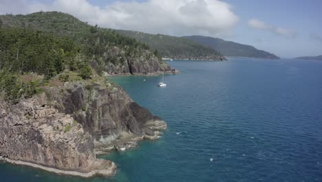 vuelo aéreo más allá de los acantilados rocosos destrozados al velero catamarán en la bahía