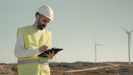 un ingeniero de energía renovable con casco blanco inspecciona turbinas eólicas en un día soleado, enfatizando la importancia de mantener generadores de energía limpia