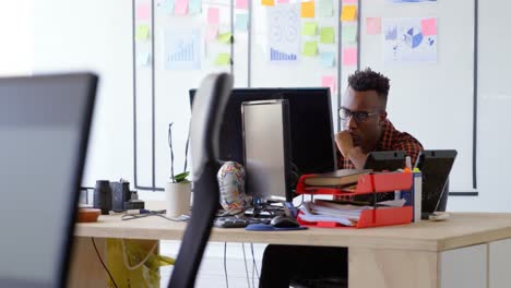 Vista-Frontal-De-Un-Joven-Hombre-De-Negocios-Negro-Pensativo-Trabajando-Y-Sentado-En-El-Escritorio-En-Una-Oficina-Moderna-4k