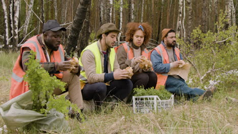 grupo de activistas ecologistas multiétnicos comiendo y hablando en un descanso sentados en un tronco en el bosque