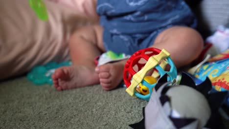 close up of 6-month-old infant playing with ball rattle, teething ring on blanket