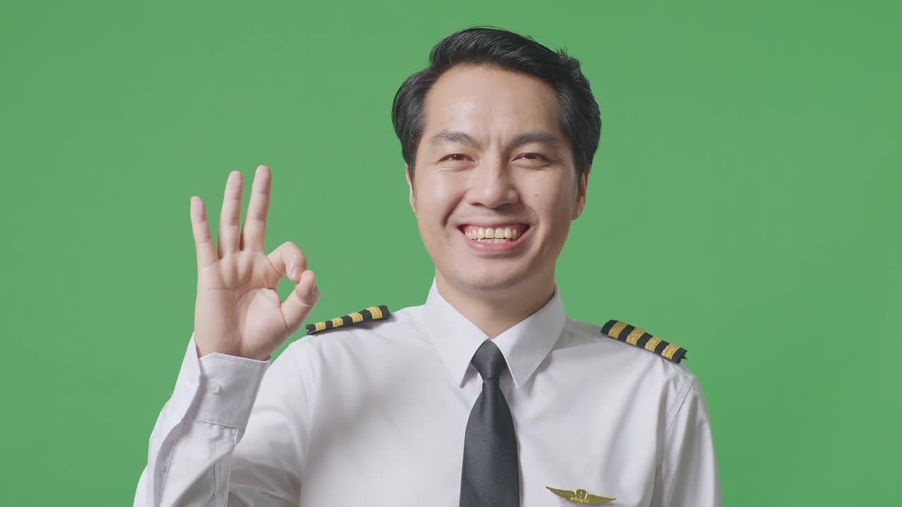 Close Up Of Asian Man Pilot Smiling And Showing Okay Gesture To Camera While Standing In The Green Screen Background Studio