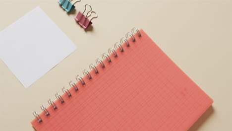 primer plano de un cuaderno rojo y artículos escolares dispuestos sobre un fondo beige, en cámara lenta