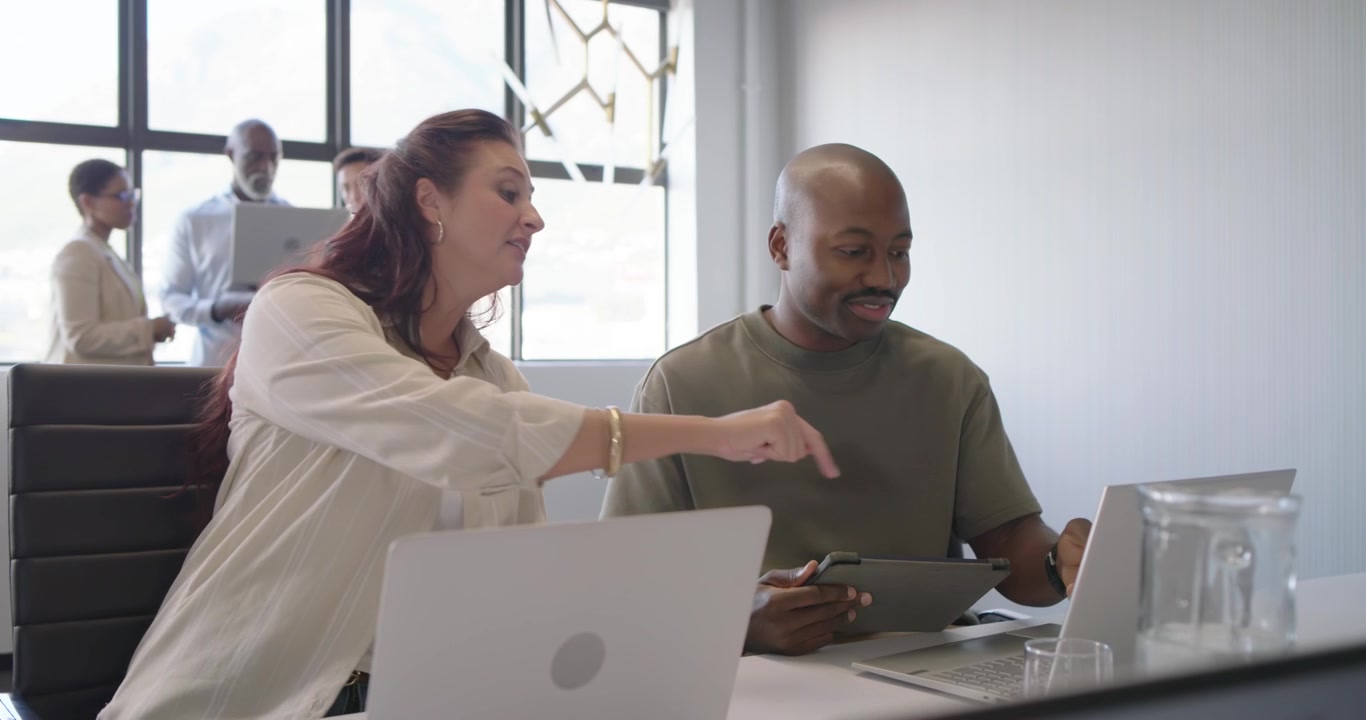 African American man and woman navigating tablet leaning at laptop working on plan in meeting room