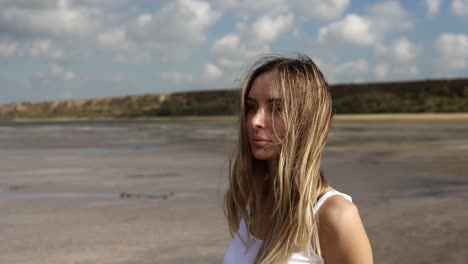 Portrait-of-a-long-haired-thoughtful-woman-standing-with-lake-on-the-background-with-blowing-wind