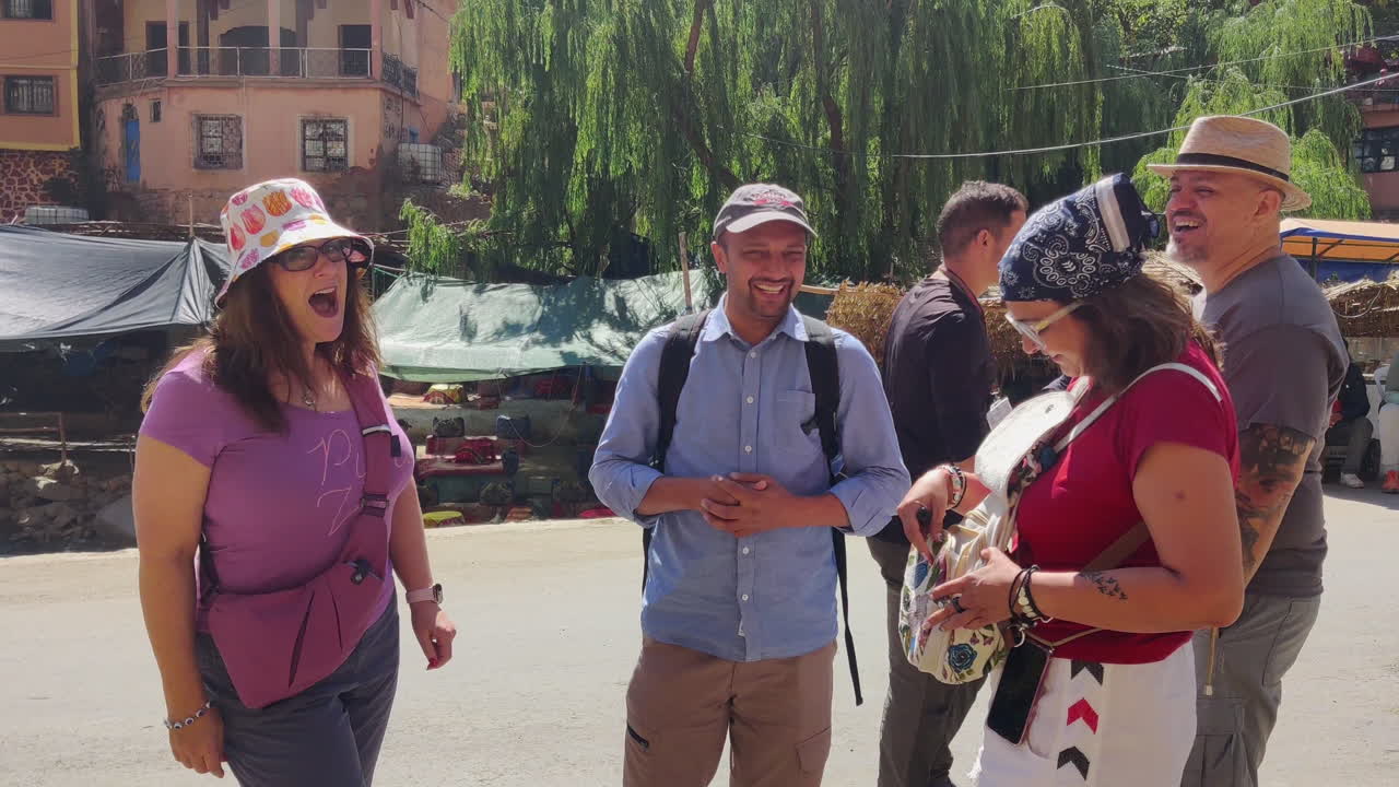 Tourists chat and laugh together in a sunny Ourika valley, enjoying a lively outdoor market