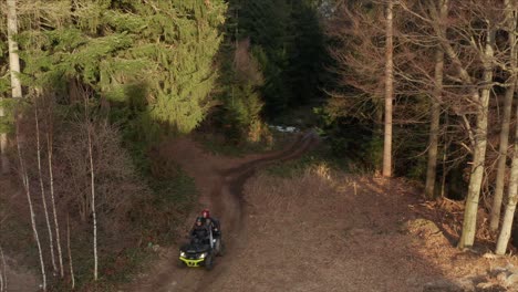 aerial boom shot of an atv rushing across a forest trail in the late afternoon