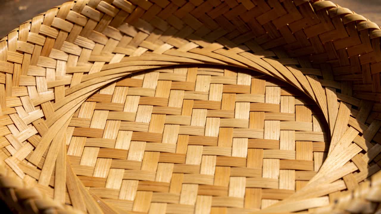 La telecamera si allontana rivelando un cesto rotondo intrecciato vuoto su un tavolo di legno a doghe, con la luce del sole che si sposta.