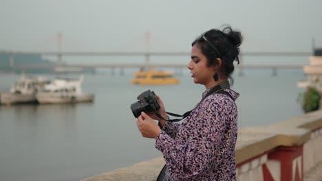 a tourist woman stands in front of a river, skillfully capturing moments with her camera as boats gently sway in the background
