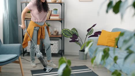 joyful housewife wearing headphones vacuuming carpet at home and dancing enjoying chores