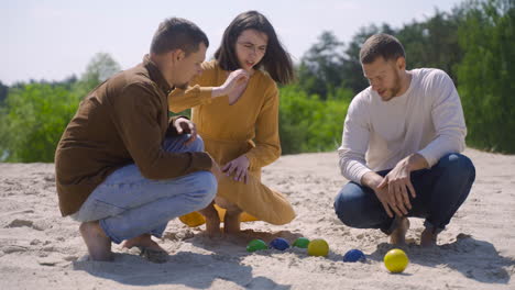 group of caucasian young friends calculating distance between petanque balls on the beach on a sunny day