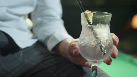 close-up of person, face not visible, wearing white shirt and grey trousers, holding glass of lemon drink with black straw. ice cubes and lemon slice