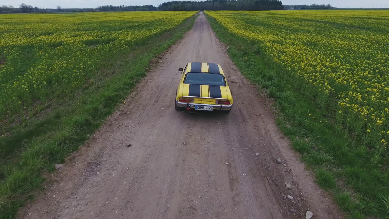 Yellow With Black Stripes Classic Ford Consul Rides On A Gravel Road. 4K Aerial Footage