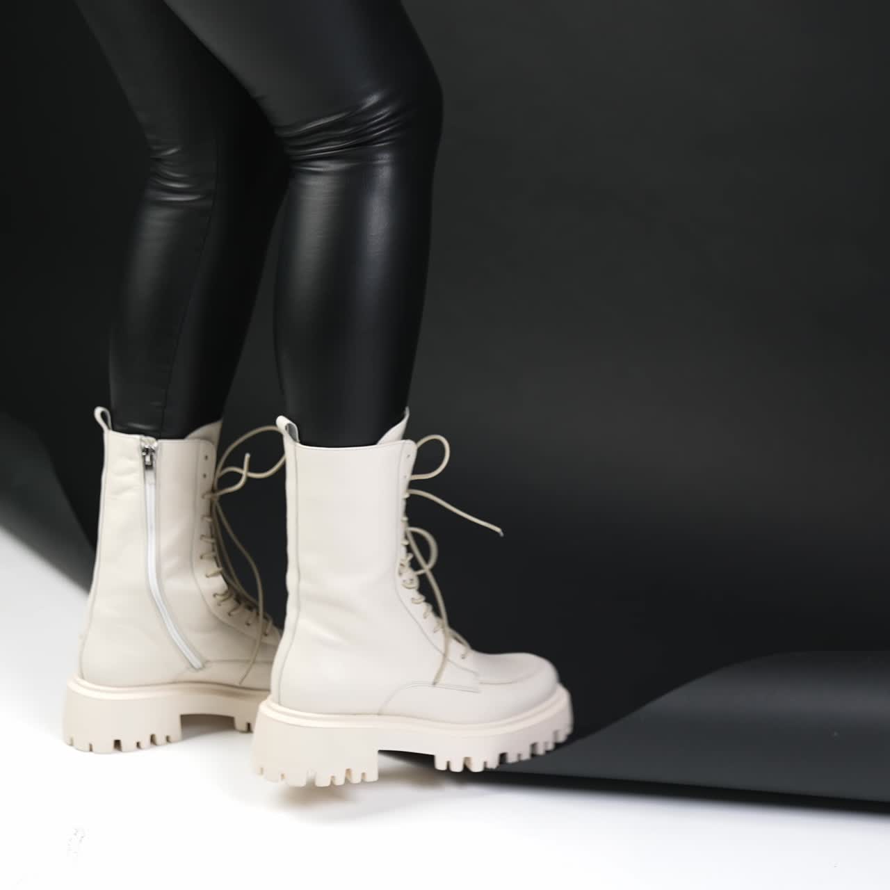 White combat boots on tractor soles. Model in black pants standing with her back to camera on a black and white backdrop