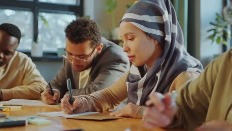 woman in hijab taking notes at desk with group mates during lecture
