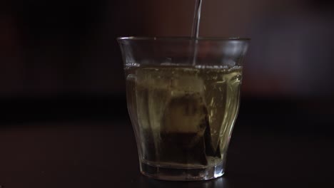 Close-up-view-of-pouring-boiled-water-into-a-glass-with-tea-bag-inside,-shallow-depth-of-field