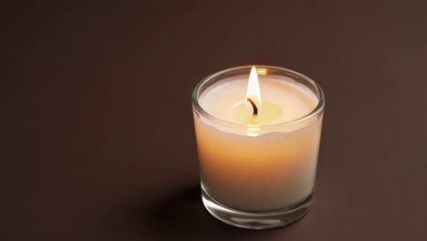 a single burning candle in a glass holder on a dark background